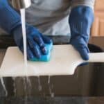 A man hand washing a chopping board in the kitchen.