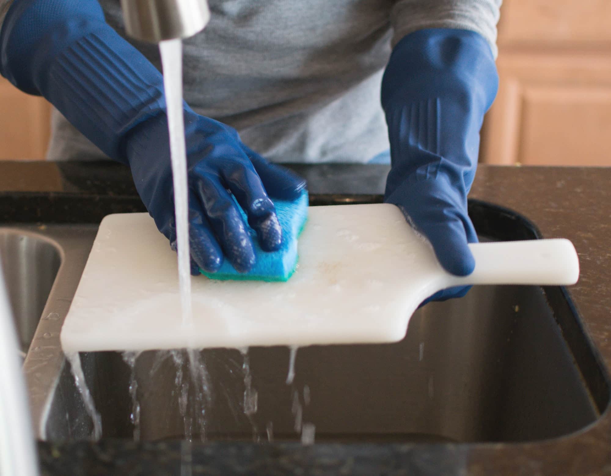A man hand washing a chopping board in the kitchen.