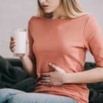 cropped view of blonde woman with lactose intolerance holding glass of milk while sitting on sofa