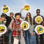 Group of happy positive friends holding discs with handdrawn emoji smiley faces standing outdoor