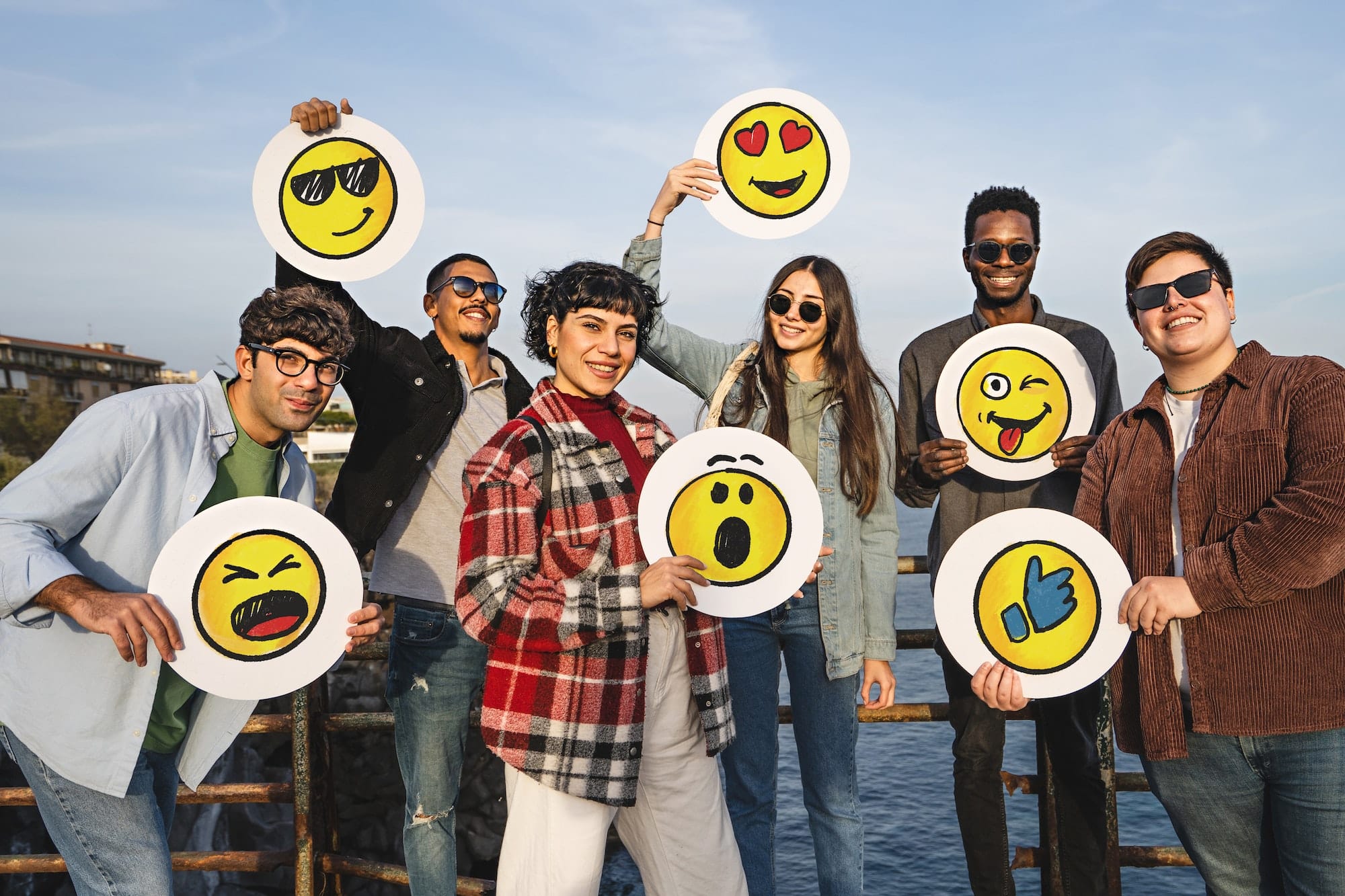Group of happy positive friends holding discs with handdrawn emoji smiley faces standing outdoor