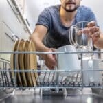 The man takes clean, washed dishes from the dishwasher.