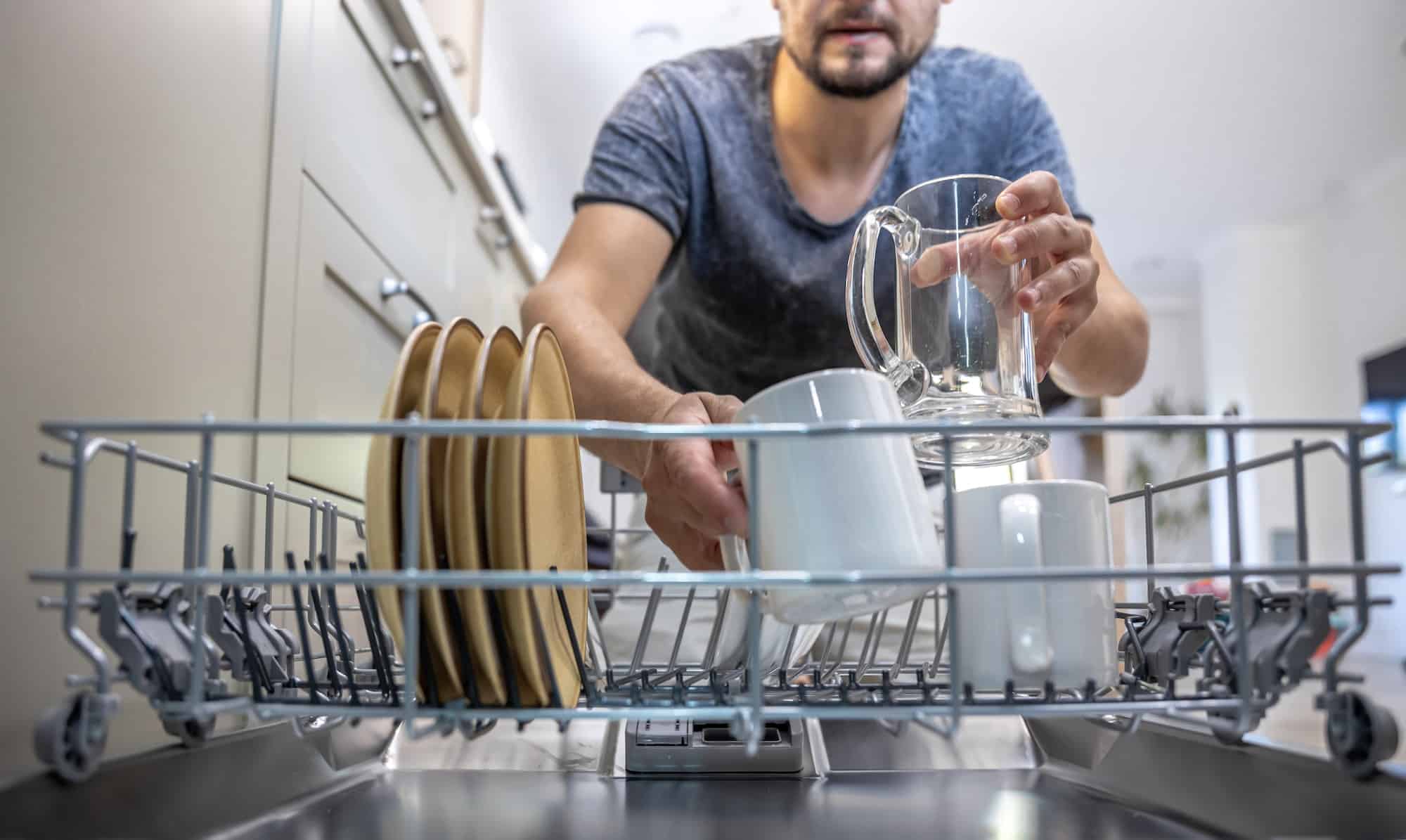 The man takes clean, washed dishes from the dishwasher.