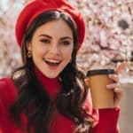 Beautiful woman in red outfit holds glass of tea and takes selfie on background of sakura. Portrait