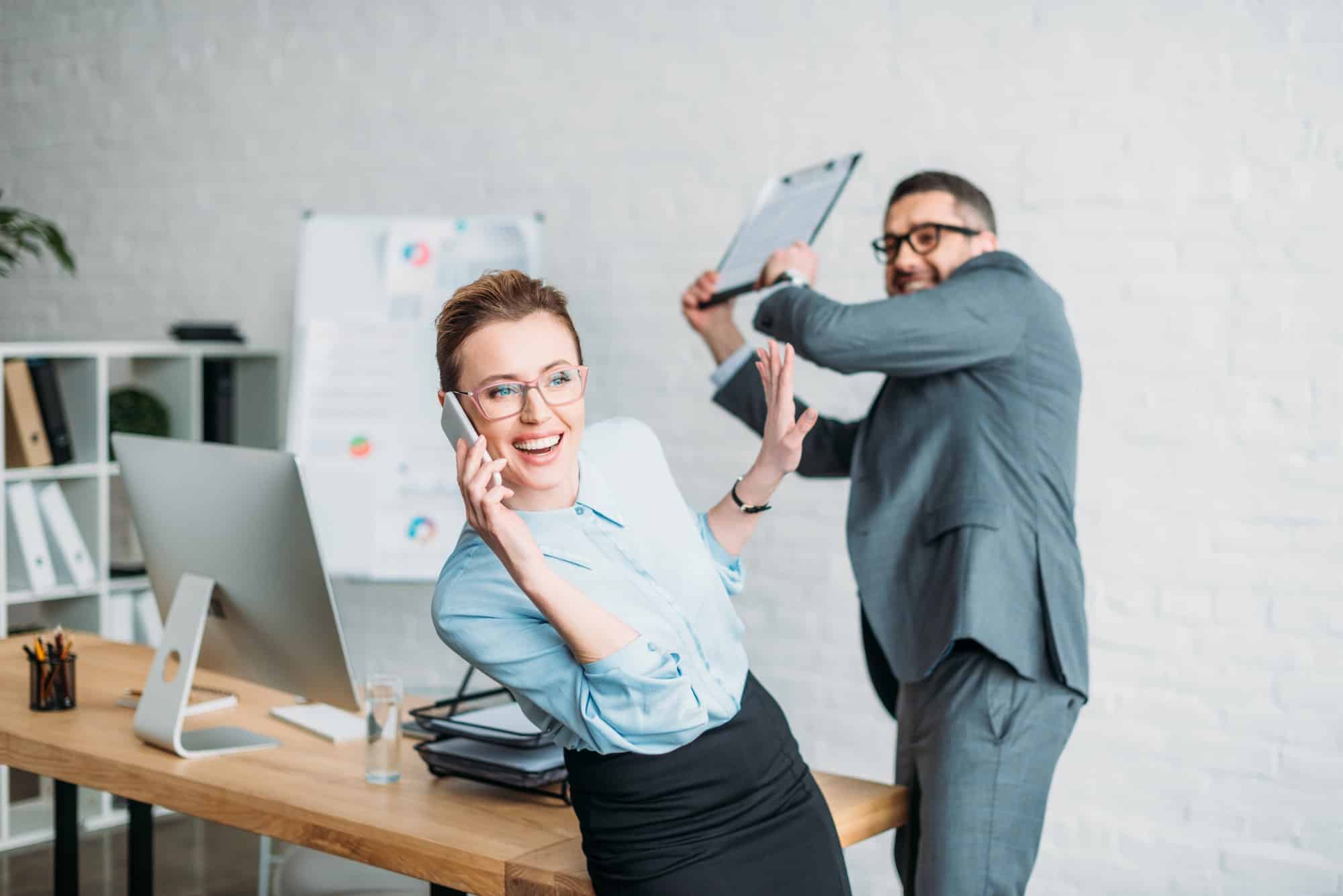 businessman get ready to hit his colleague with clipboard while she talking by phone and annoying