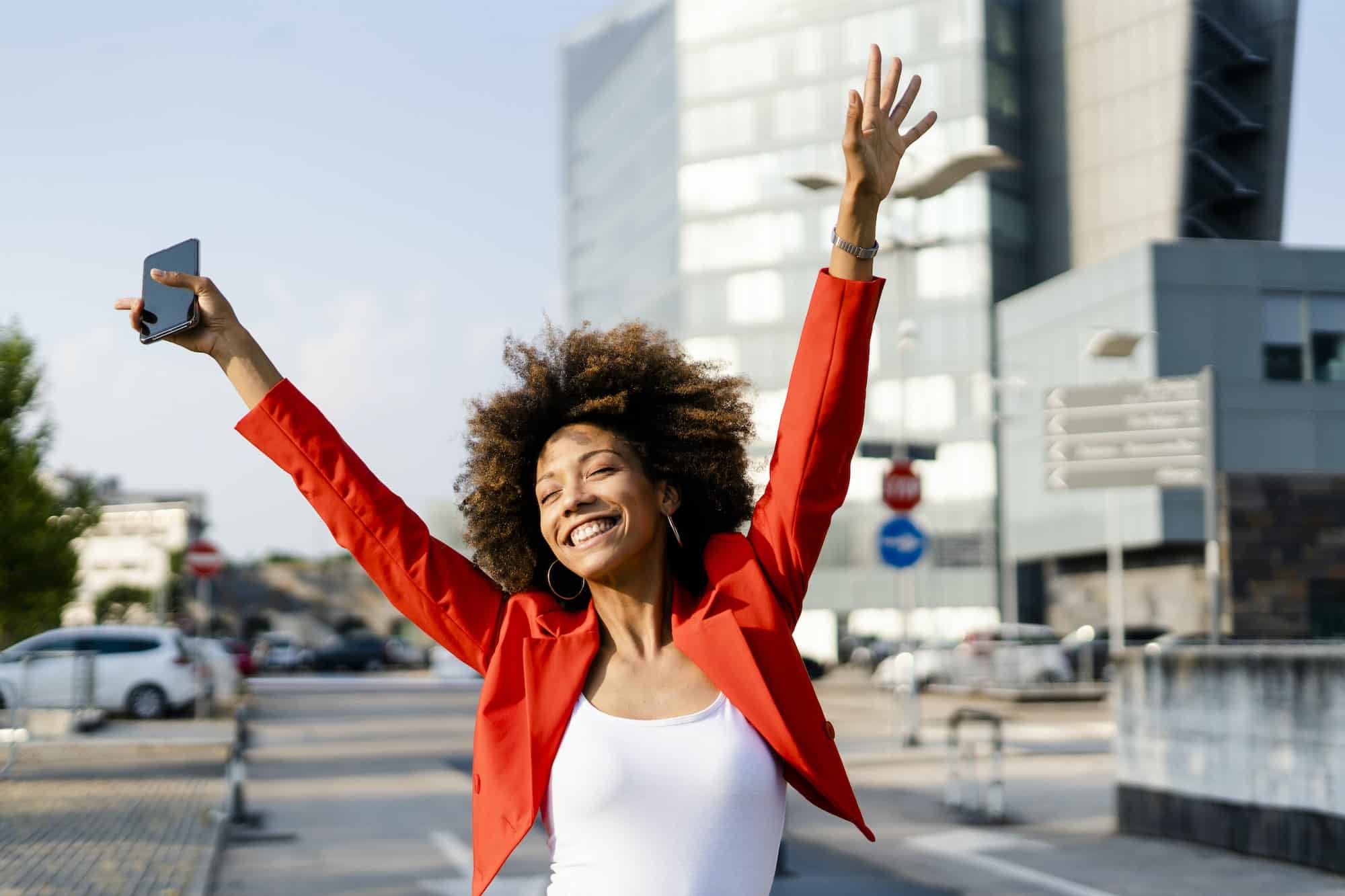 Portrait of happy young woman with smartphone wearing fashionable red suit jacket