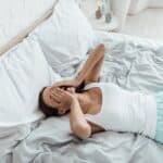 stressed young woman covering face with hands and crying in bed