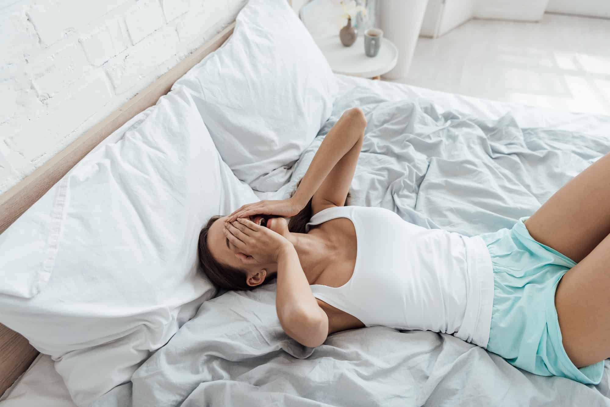 stressed young woman covering face with hands and crying in bed