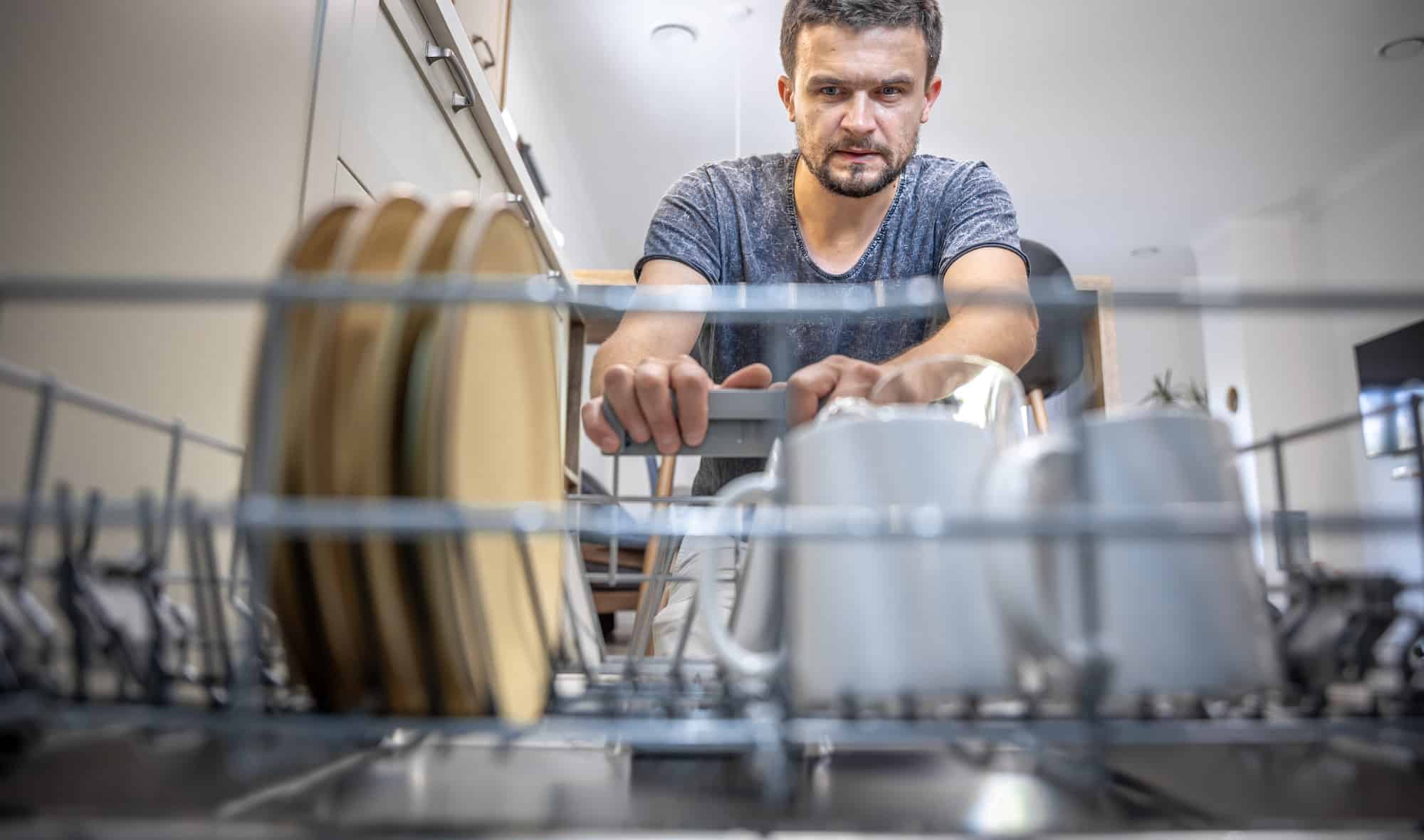 The man looks at the washed dishes from the dishwasher.