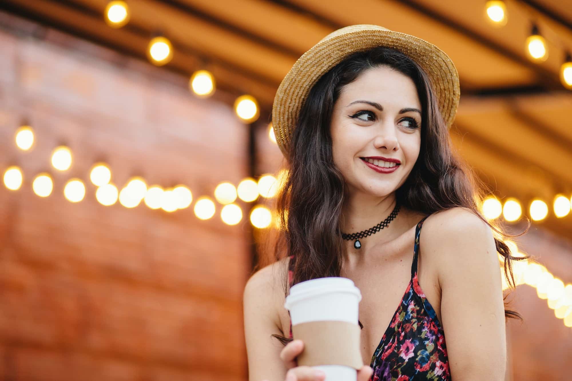 Shy brunette female with dark eyes and red lips wearing straw hat and dress