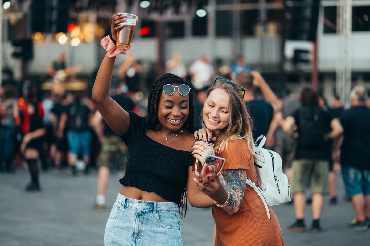 amis utilisant un smartphone et buvant du soda lors d'un festival de musique