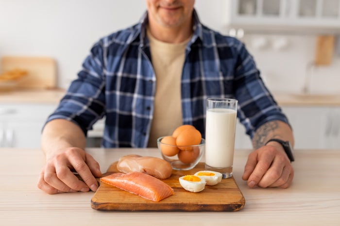 concept de régime protéiné. homme âgé assis à la table de la cuisine avec du lait en verre, de la viande crue et du filet de saumon, des œufs, en gros plan