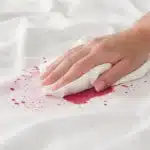 Main tamponnant une nappe blanche tachée de vin rouge avec un essuie-tout pour absorber rapidement sans frotter