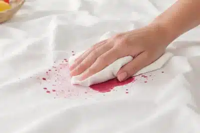 Main tamponnant une nappe blanche tachée de vin rouge avec un essuie-tout pour absorber rapidement sans frotter