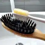 Main nettoyant une brosse à cheveux dans de l’eau tiède savonneuse avec une vieille brosse à dents pour retirer les résidus.