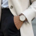 Personne élégante portant une montre classique au poignet gauche, tenue chic et lumière naturelle